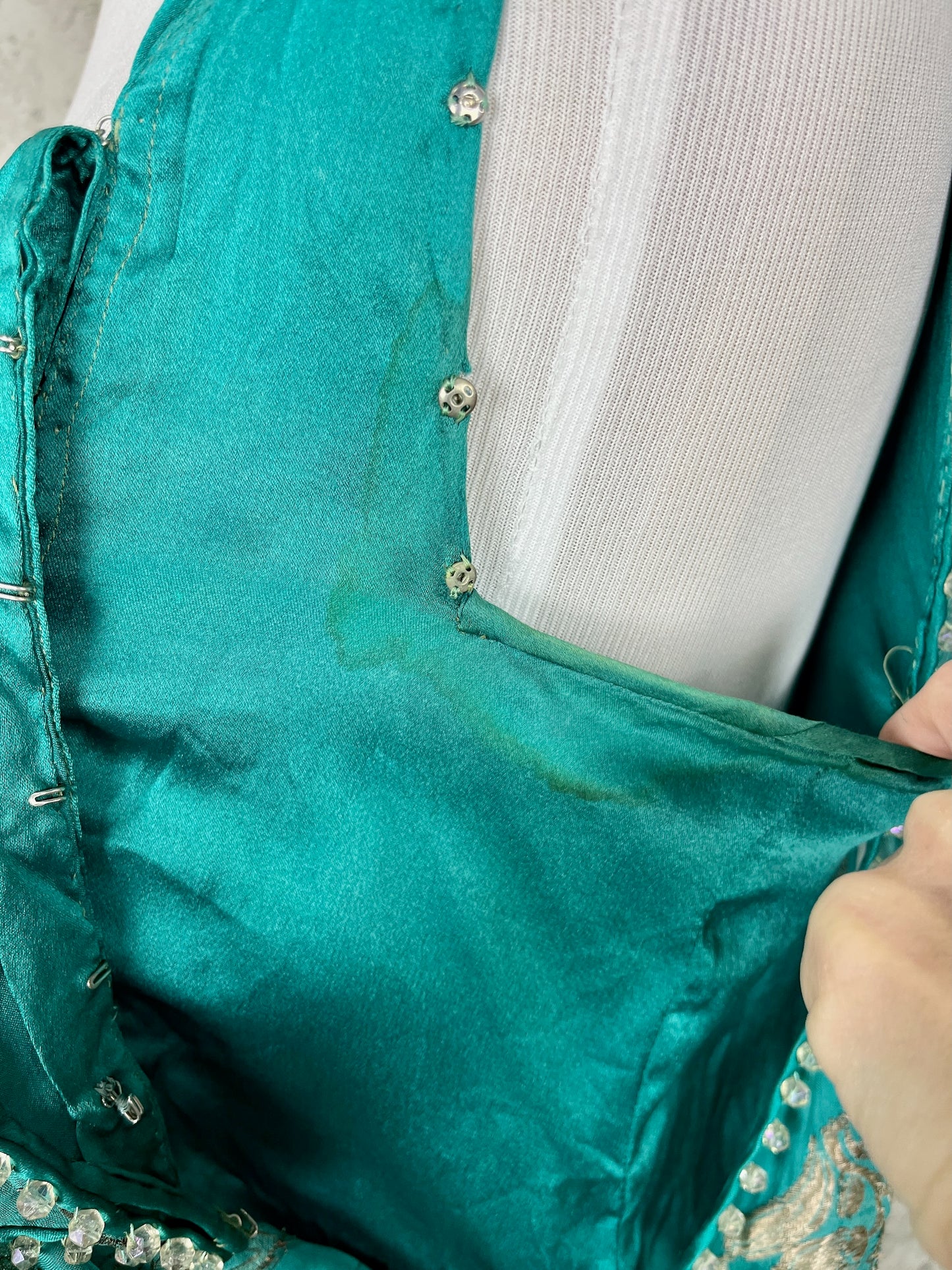 close-up of left underarm of solid teal under lining showing underarm discoloration and snaps that lame over layer fasten onto
